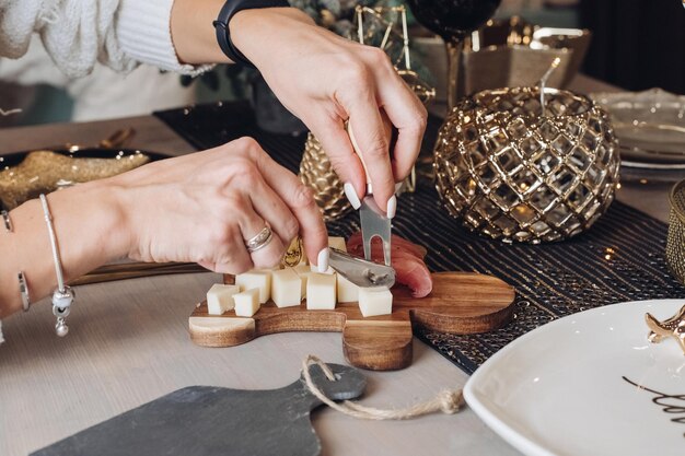 Foto recortada de mujer probando queso sobre una tabla de madera con adornos navideños en el fondo