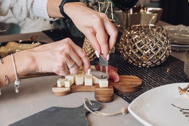 Foto recortada de mujer probando queso sobre una tabla de madera con adornos navideños en el fondo