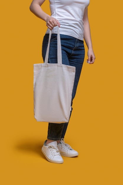 Foto gratuita foto recortada de una mujer vestida con una camiseta y jeans sosteniendo su bolso moderno en una mano