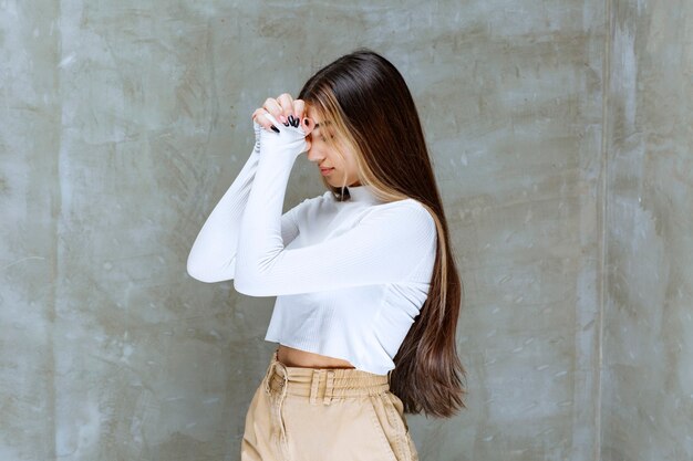 Foto de retrato de un modelo de niña sonriente de pie y rezando contra la piedra