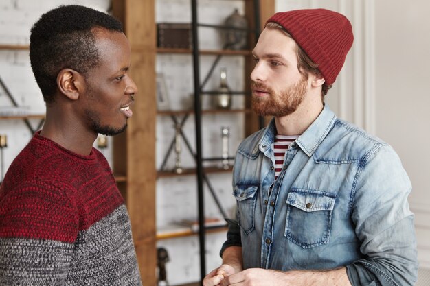 Foto sincera de dos mejores amigos masculinos con estilo de diferentes razas de pie uno frente al otro