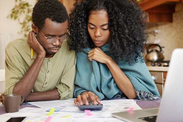 Foto sincera de pareja africana estresada revisando sus finanzas en casa