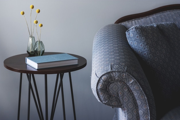 Foto gratuita foto de un sofá azul cerca de una pequeña mesa redonda con un libro y dos jarrones con plantas amarillas