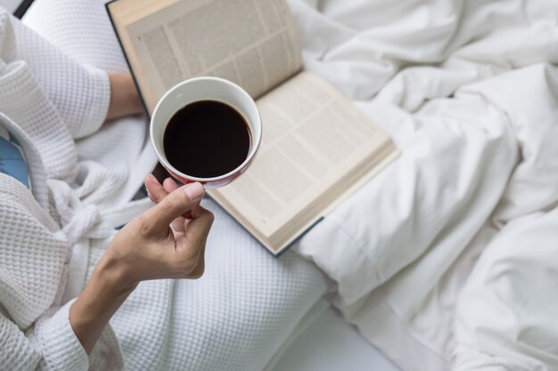 Foto suave de la mujer en la cama con libro antiguo y una taza de café y copia espacio.