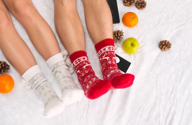 Foto gratuita foto suave de mujer y hombre en la cama con teléfono y frutas, punto de vista superior. piernas femeninas y masculinas de pareja en cálidos calcetines de lana.