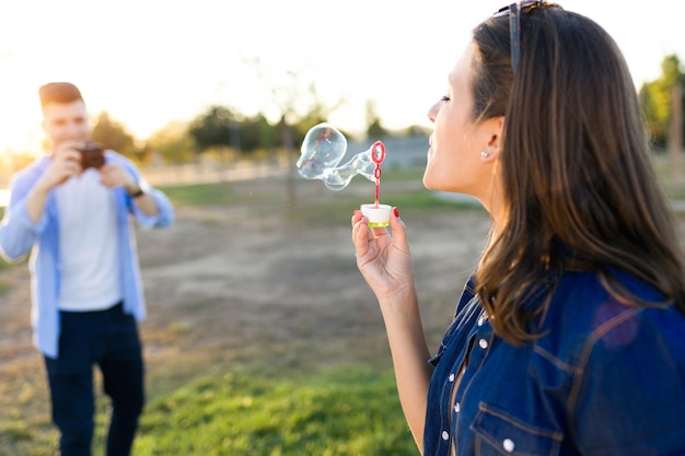 Foto de toma joven guapo de su novia haciendo pompas de jabón en el parque.