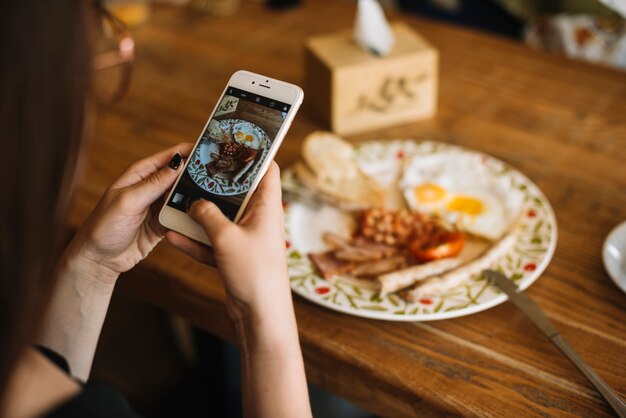 Foto de toma de la mano de la mujer del desayuno en la mesa de madera a través del teléfono celular