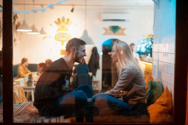 Foto a través de la ventana. Pareja joven en café con interior elegante