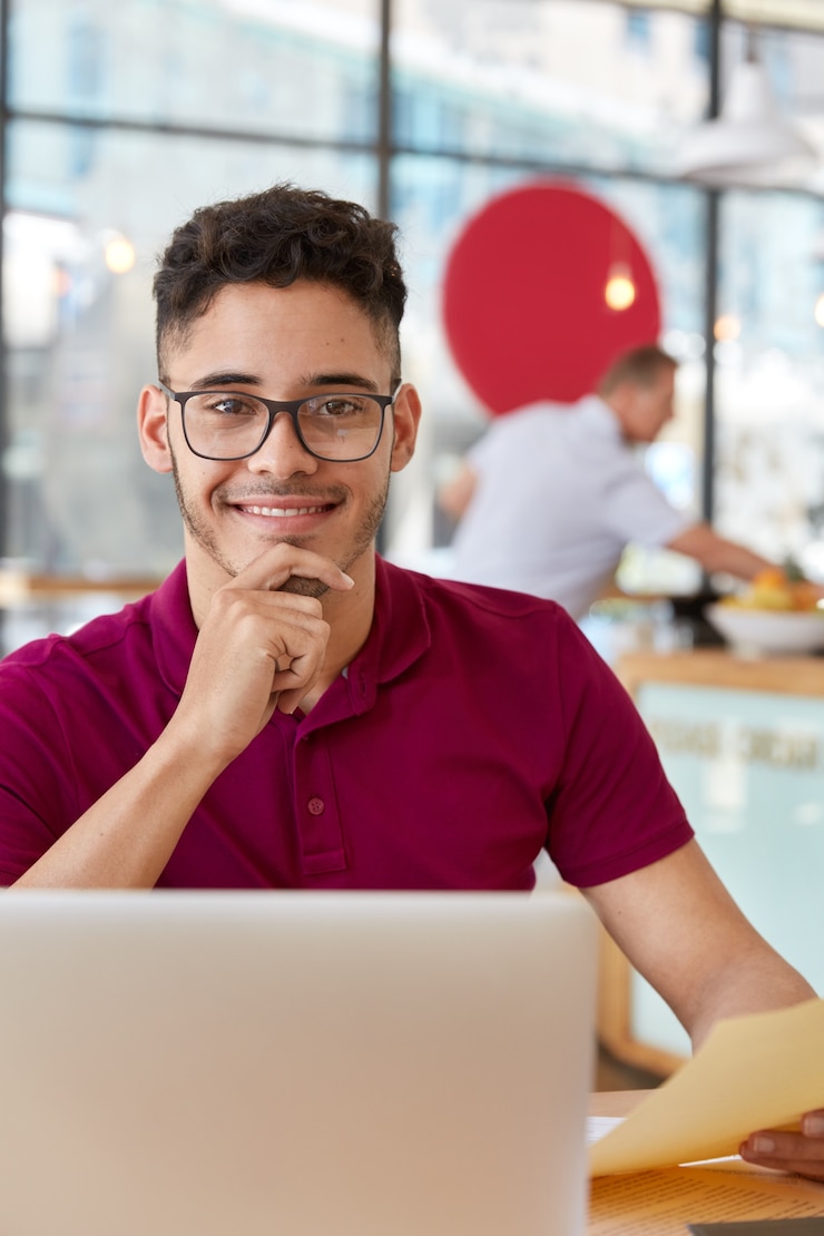 Foto gratuito foto veética del desarrollador de software que adapta la aplicación a la plataforma del sistema, trabaja en una computadora portátil, escucha la documentación, sostiene la barbilla, usa anteojos, camiseta informal, charla sobre algunas ideas.