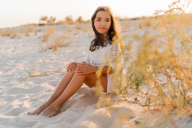 Foto de verano de una niña pequeña con un elegante atuendo boho posando en la playa Colores cálidos del atardecer Concepto de vacaciones y viajes