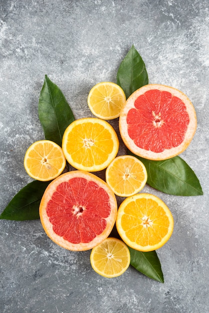 Foto vertical de frutas cítricas frescas, frutas cortadas a la mitad con hojas sobre la superficie gris.