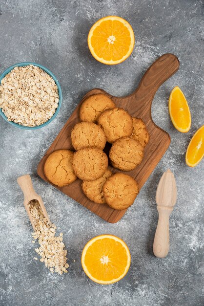 Foto vertical de galletas caseras con avena y rodajas de naranja sobre tabla gris.