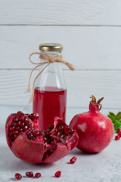 Foto vertical de granadas en rodajas o enteras con una botella de jugo.