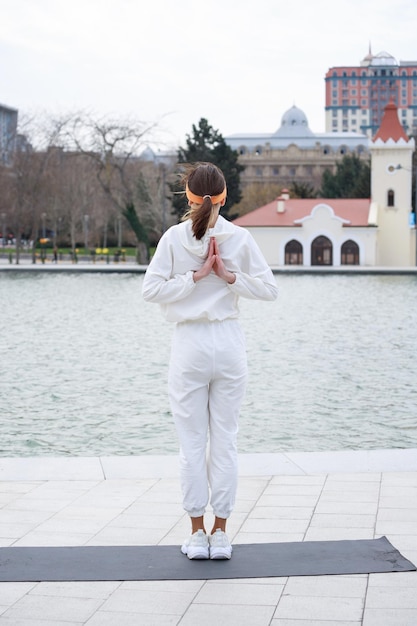 Foto vertical de una joven atleta parada en una alfombra de yoga y sosteniendo sus manos hacia atrás Foto de alta calidad