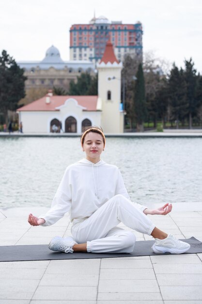 Foto vertical de un joven atleta sentado en una alfombra de yoga y haciendo meditación en el parque Foto de alta calidad