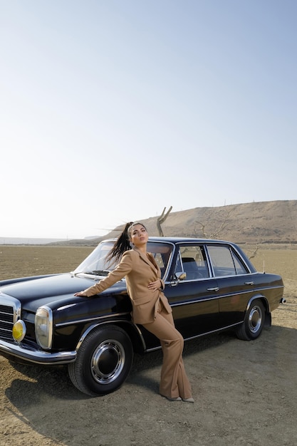 Foto vertical de una joven hermosa con auto en el desierto Foto de alta calidad