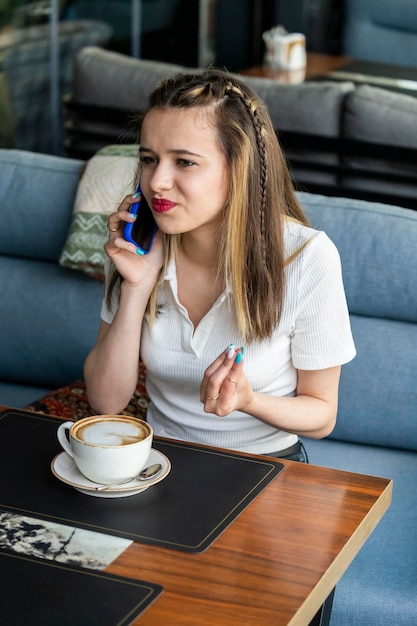 Foto vertical de una joven hermosa hablando por teléfono y sentada en el restaurante