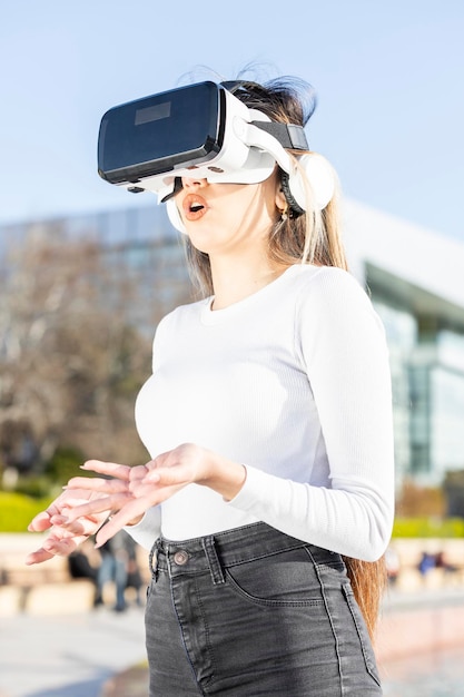 Foto vertical de una joven que usa gafas de realidad virtual y se para en la calle
