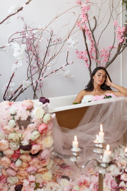 Foto vertical de una joven sentada en una bañera alrededor de velas y flores Foto de alta calidad