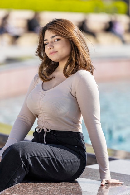 Foto vertical de una joven sentada en el parque y mirando a la cámara Foto de alta calidad