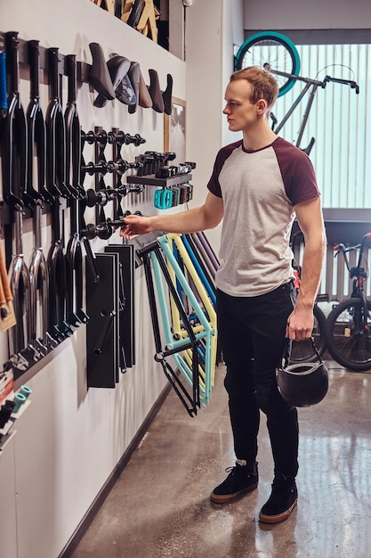 Foto vertical de un joven sosteniendo un casco protector y eligiendo piezas para su BMX en una tienda de bicicletas