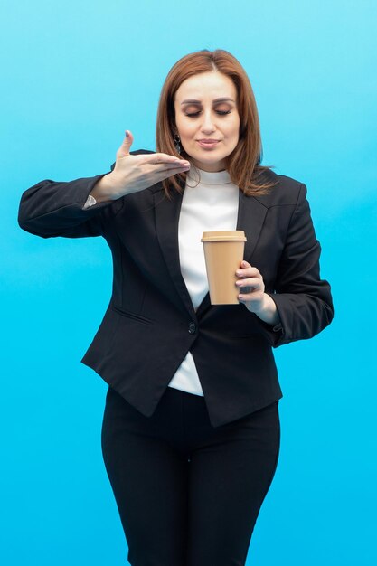 Foto vertical de una joven sosteniendo una taza de café y apuntándola con la mano