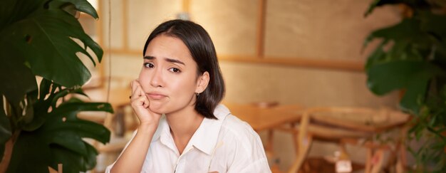 Foto vertical de una joven triste y sombría sentada con una computadora portátil en un café haciendo muecas y luciendo molesta