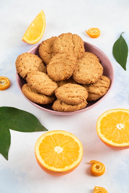 Foto vertical del montón de galletas en un tazón y naranjas medio cortadas.