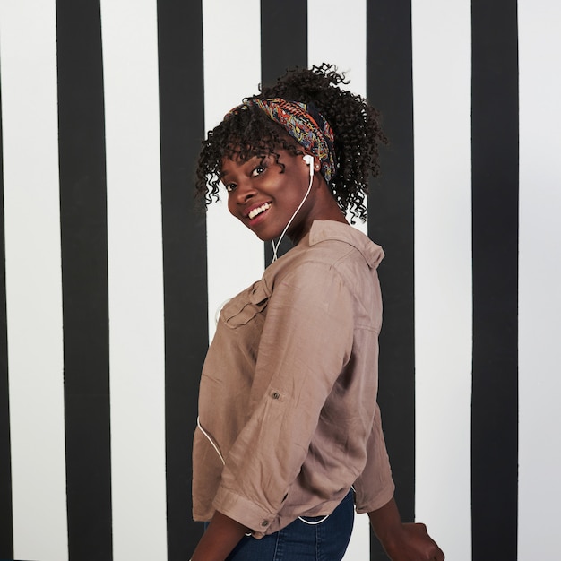 Foto vertical. niña afroamericana sonrió se encuentra en el estudio con líneas verticales blancas y negras en el fondo