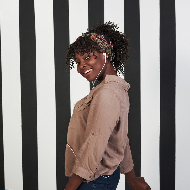 Foto vertical. Niña afroamericana sonrió se encuentra en el estudio con líneas verticales blancas y negras en el fondo