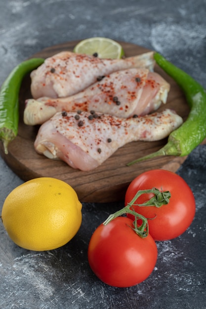 Foto vertical de tomates orgánicos frescos y limón con muslos de pollo crudo.