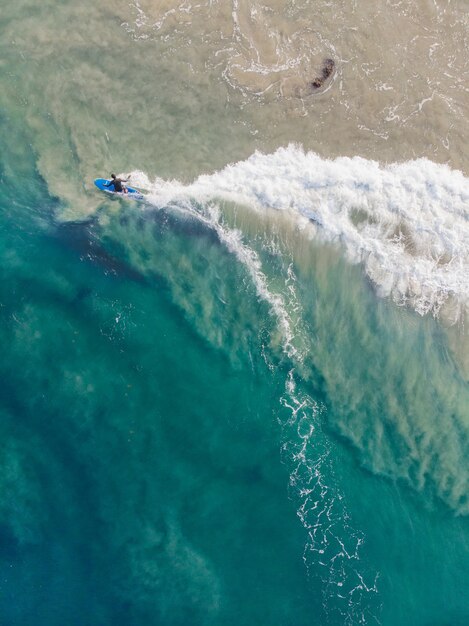 Foto de vista superior de una persona con una tabla de surf nadando en la playa de Varkala