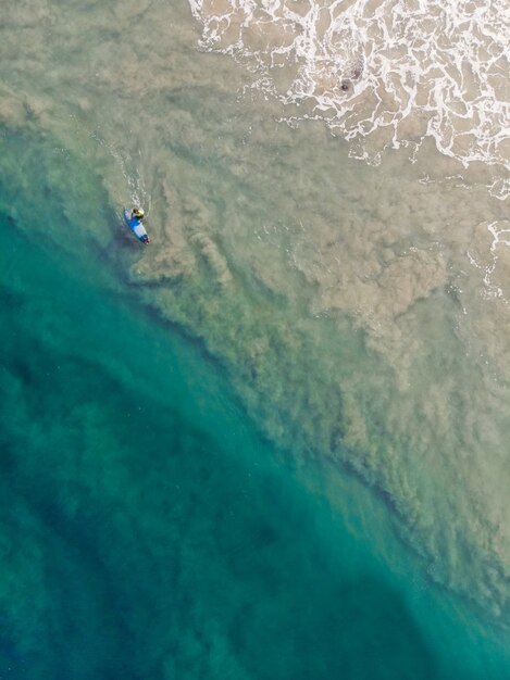 Foto de vista superior de una persona con una tabla de surf nadando en la playa de Varkala