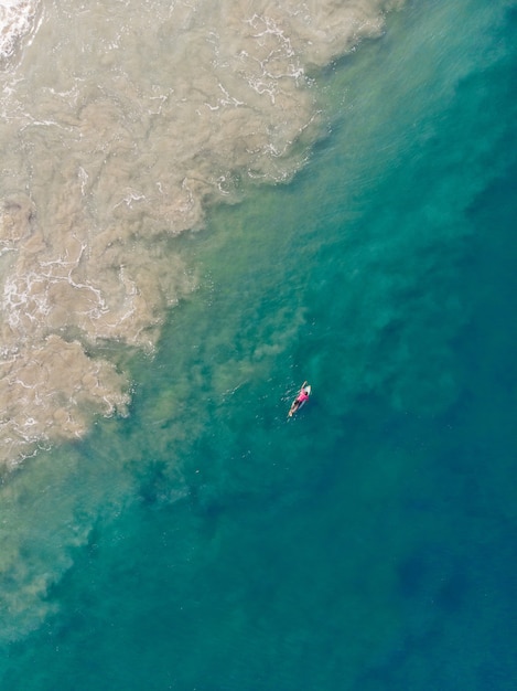 Foto de vista superior de una persona con una tabla de surf nadando en la playa de Varkala