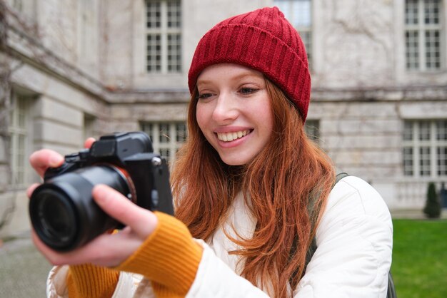 La fotógrafa pelirroja toma fotos con una cámara profesional al aire libre captura tomas de streetstyle lo