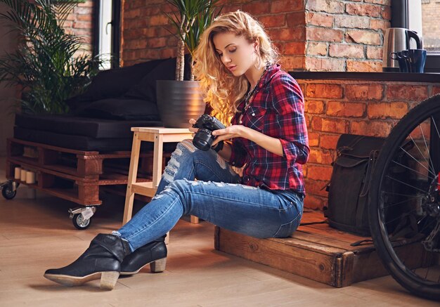 Fotógrafa rubia aficionada vestida con jeans y camisa polar tomando fotos en una habitación con interior tipo loft.