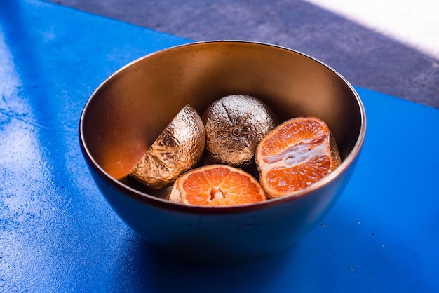 Foto gratuita fotografía abstracta de mandarinas chapadas en metal en un recipiente sobre una superficie azul y madera