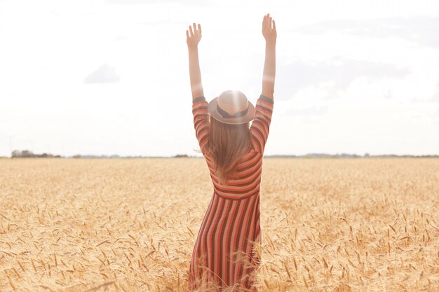 Fotografía al aire libre de una mujer joven alta y positiva que levanta sus brazos hacia el sol