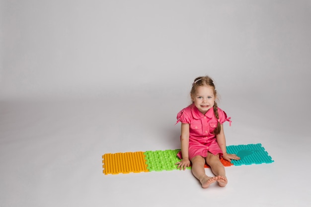 Fotografía de archivo de una niña jugando con almohadillas de goma coloridas y brillantes para mejorar y desarrollar habilidades motoras finas en el suelo. Está sentada en cuclillas en el estudio.