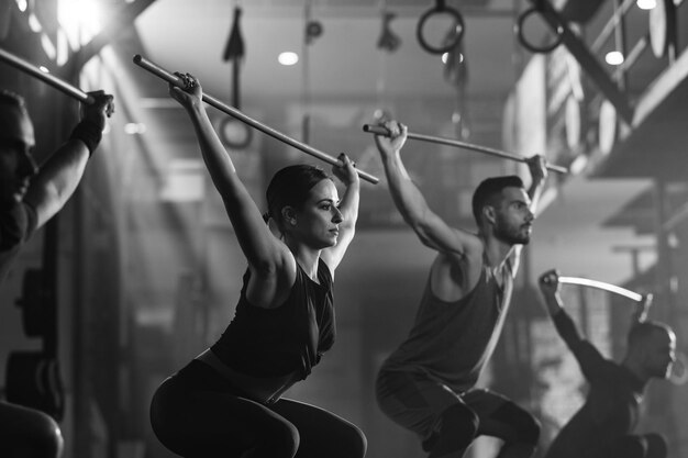 Fotografía en blanco y negro de personas atléticas haciendo ejercicio con varillas en entrenamiento cruzado en un gimnasio