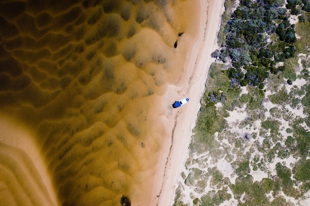 Fotografía cenital aérea de un barco en la orilla con árboles en el lado derecho