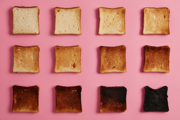 Fotografía cenital aislada de tostadas de pan en diferentes etapas de tueste contra un fondo rosado. La última rebanada está completamente quemada. Refrigerio para el desayuno. De tostado a carbonizado. Fotografía gastronómica