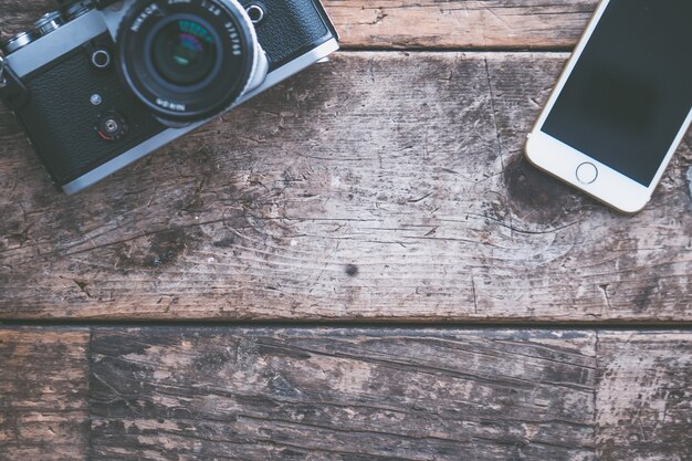 Fotografía cenital de una cámara y un teléfono inteligente sobre un fondo de madera marrón