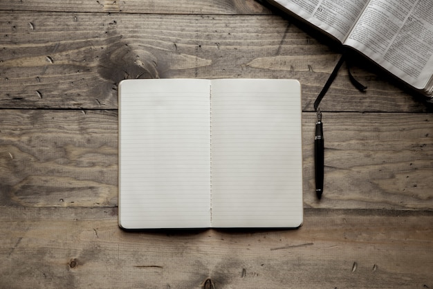 Fotografía cenital de un cuaderno en blanco cerca de una pluma estilográfica sobre una superficie de madera