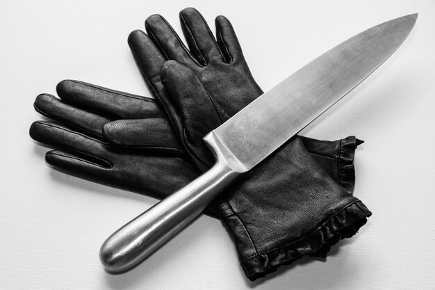Fotografía cenital de un cuchillo de metal sobre guantes negros sobre una superficie blanca