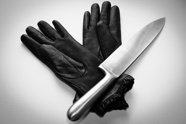 Fotografía cenital de un cuchillo de metal sobre guantes negros sobre una superficie blanca