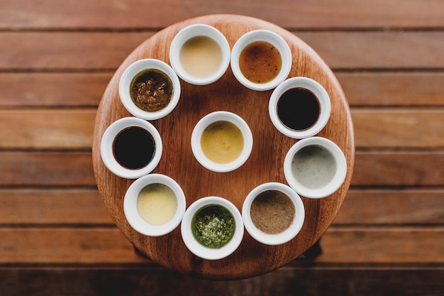 Fotografía cenital de diez cuencos blancos con diferentes salsas y especias alineados en un taburete