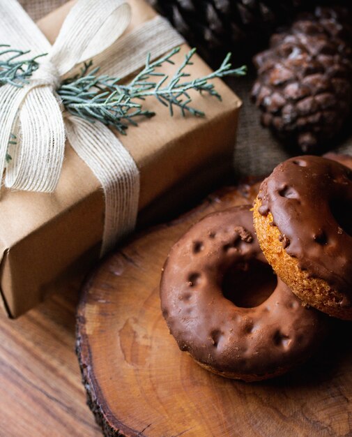 Fotografía cenital de donas bañadas en chocolate sobre tabla de madera junto a una caja de regalo envuelta