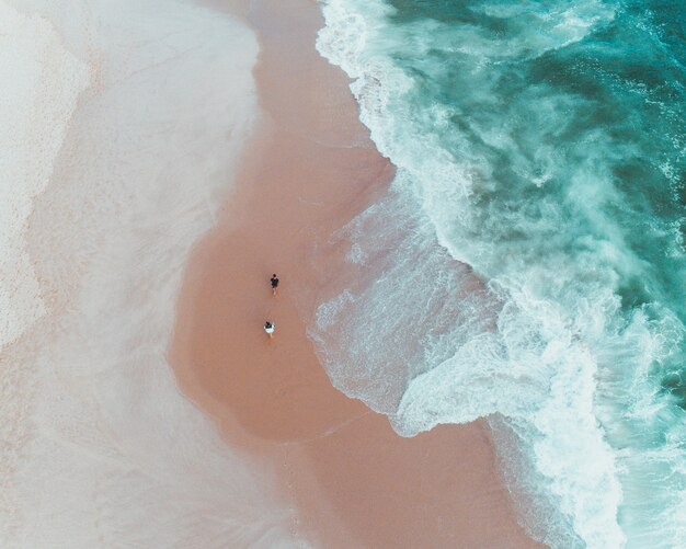 Fotografía cenital de gente disfrutando de un día soleado en una playa de arena cerca de hermosas olas del mar