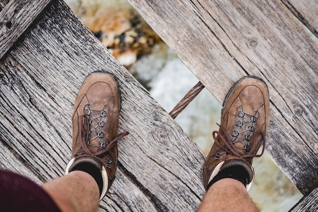 Fotografía cenital de un hombre pies de pie sobre un puente de madera con zapatos de senderismo
